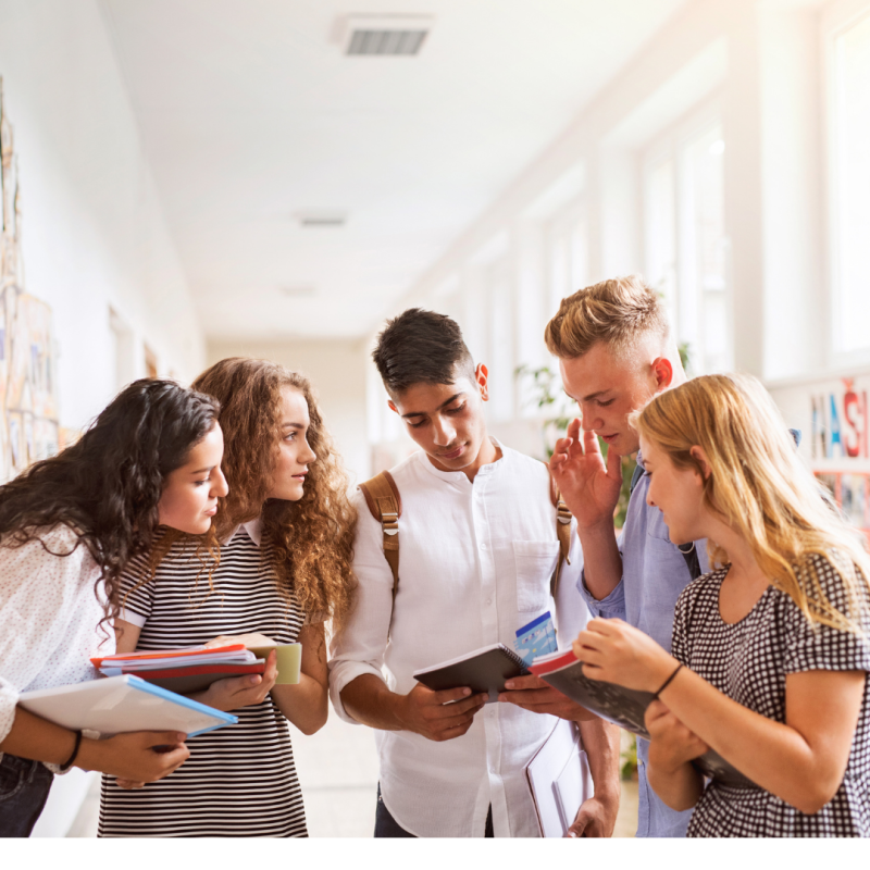Five friends looking at their notebooks in hallway.