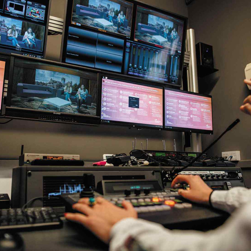 2 peoples hands only on keyboard / control panel in TV production room, with multiple screens in front of them.