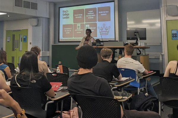 Presenter at front of classroom, screen says 'Kings College London'